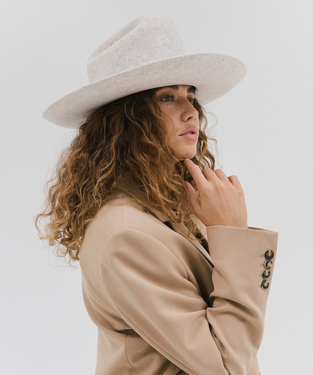Woman wearing a mix grey colored Western hat with a classic cattleman crown, and a beige coat, looking sideways against a plain background  #color_mix grey