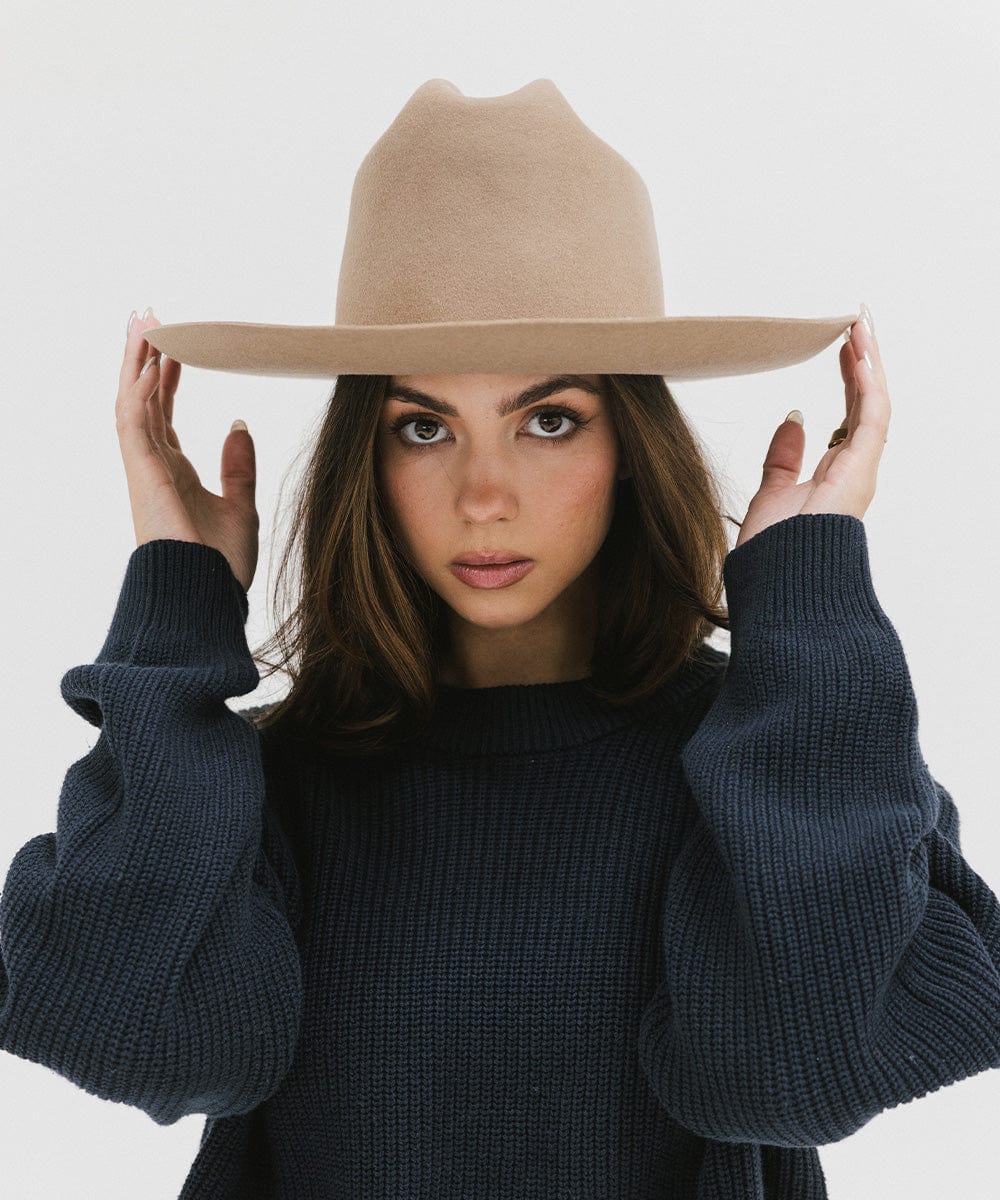 Woman wearing a tan Western hat with a classic cattleman crown, and a dark blue sweatshirt against a plain background  #color_tan