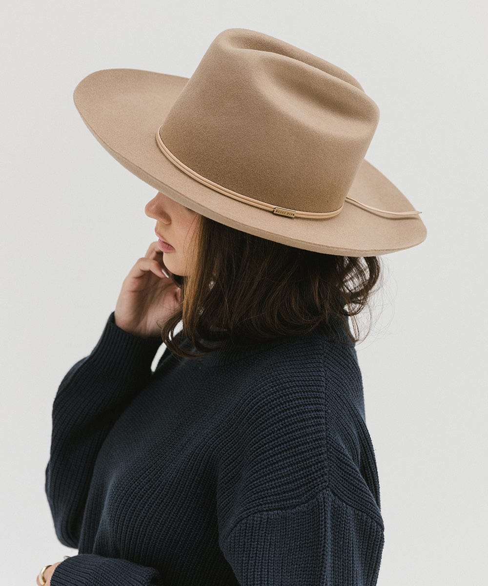 Woman wearing a tan Western hat with a classic cattleman crown and a hat band, and a dark blue sweatshirt, facing sideways against a plain background  #color_tan