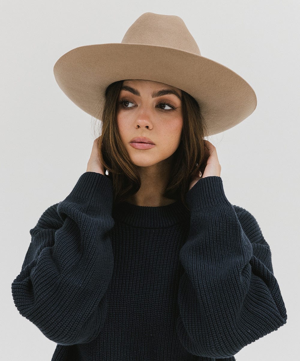 Woman wearing a tan Western hat with a classic cattleman crown, and a dark blue sweatshirt against a plain background  #color_tan