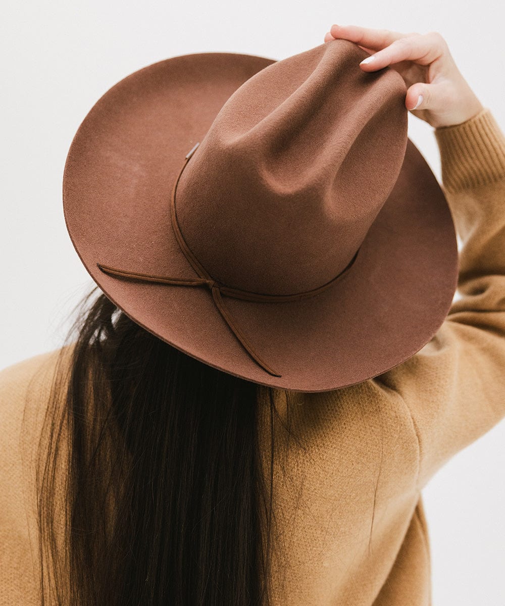 Person with long hair wearing a dark oak colored Western hat with a classic cattleman crown and a hat band, facing behind against a plain background  #color_dark oak