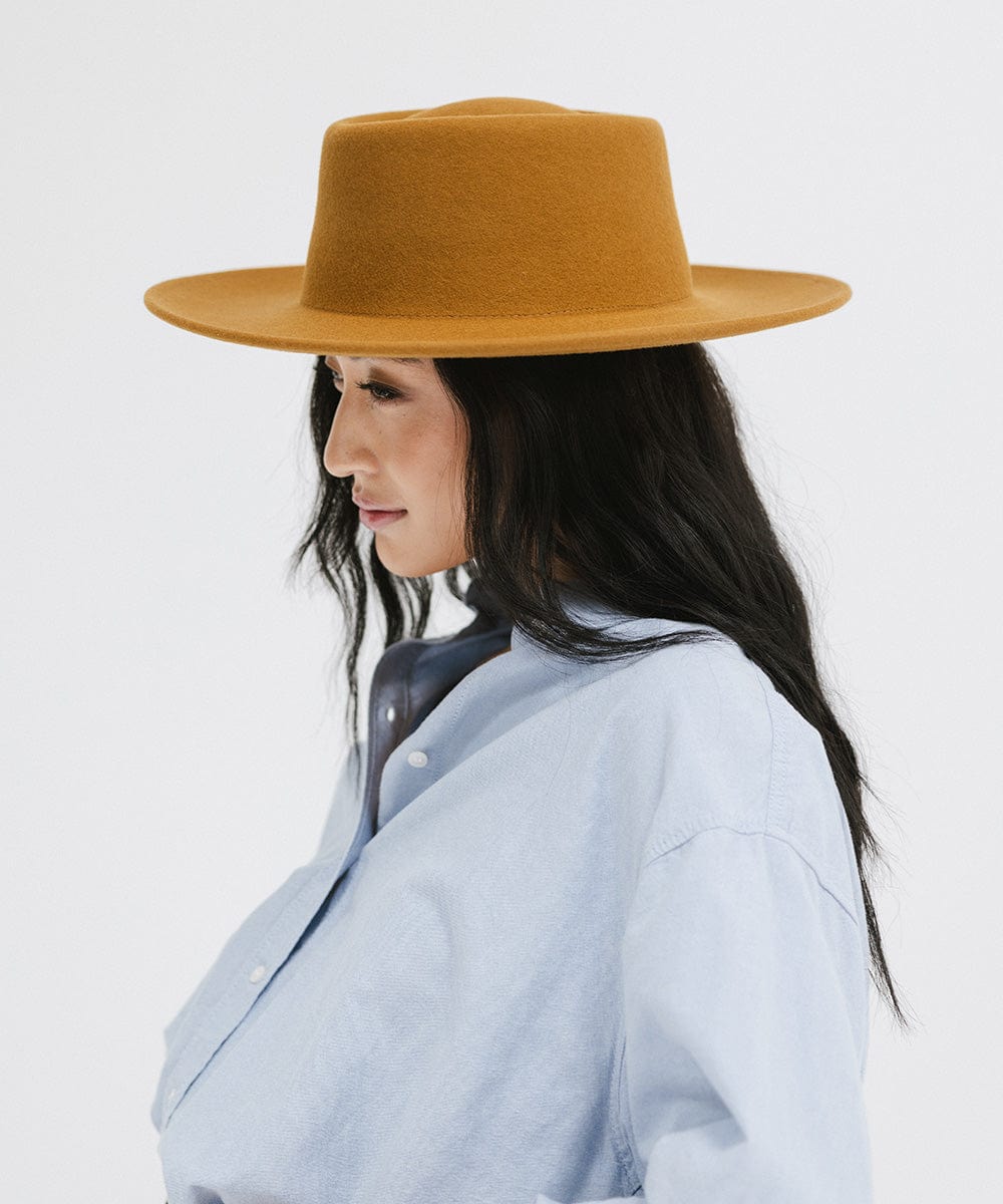 Woman wearing a cinnamon colored gambler hat and a blue shirt, facing sideways against a plain background #color_cinnamon