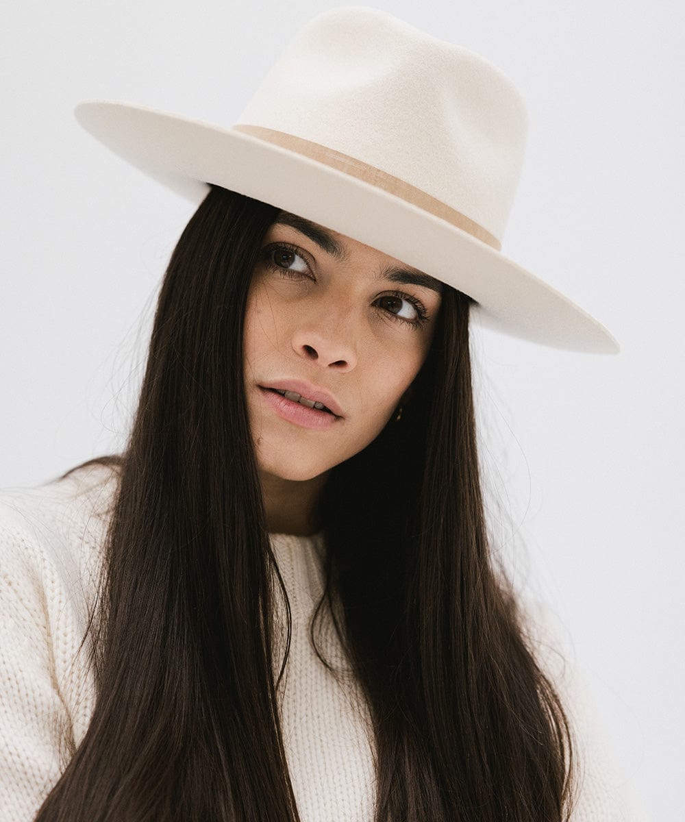 Woman wearing an off white felt fedora hat against a plain background  #color_off white