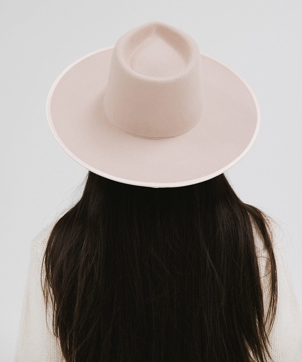 Person with long hair wearing a pale nude colored fedora hat against a plain background #color_pale nude