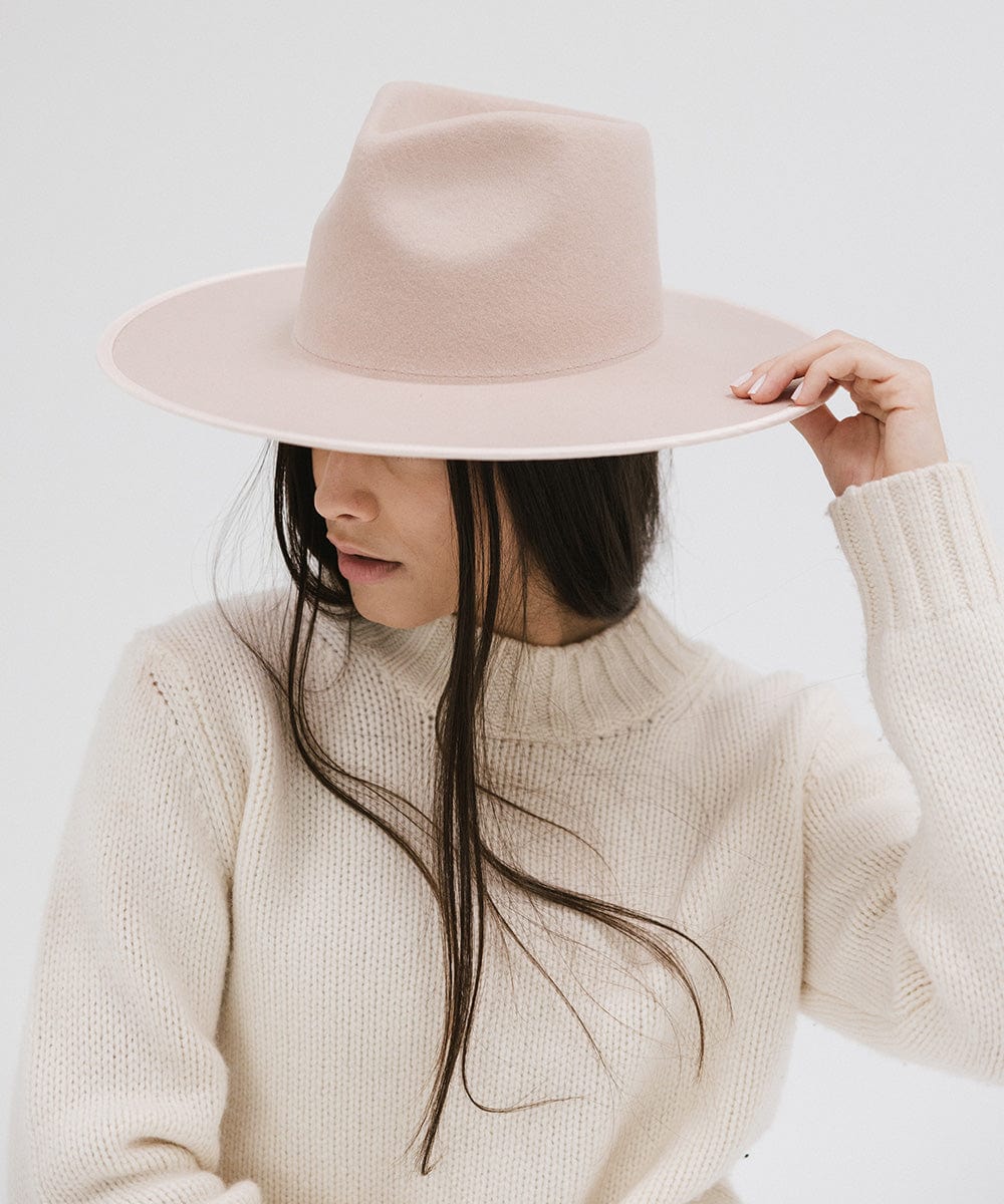 Woman wearing a pale nude colored fedora hat and a white sweater, posing against a plain background #color_pale nude