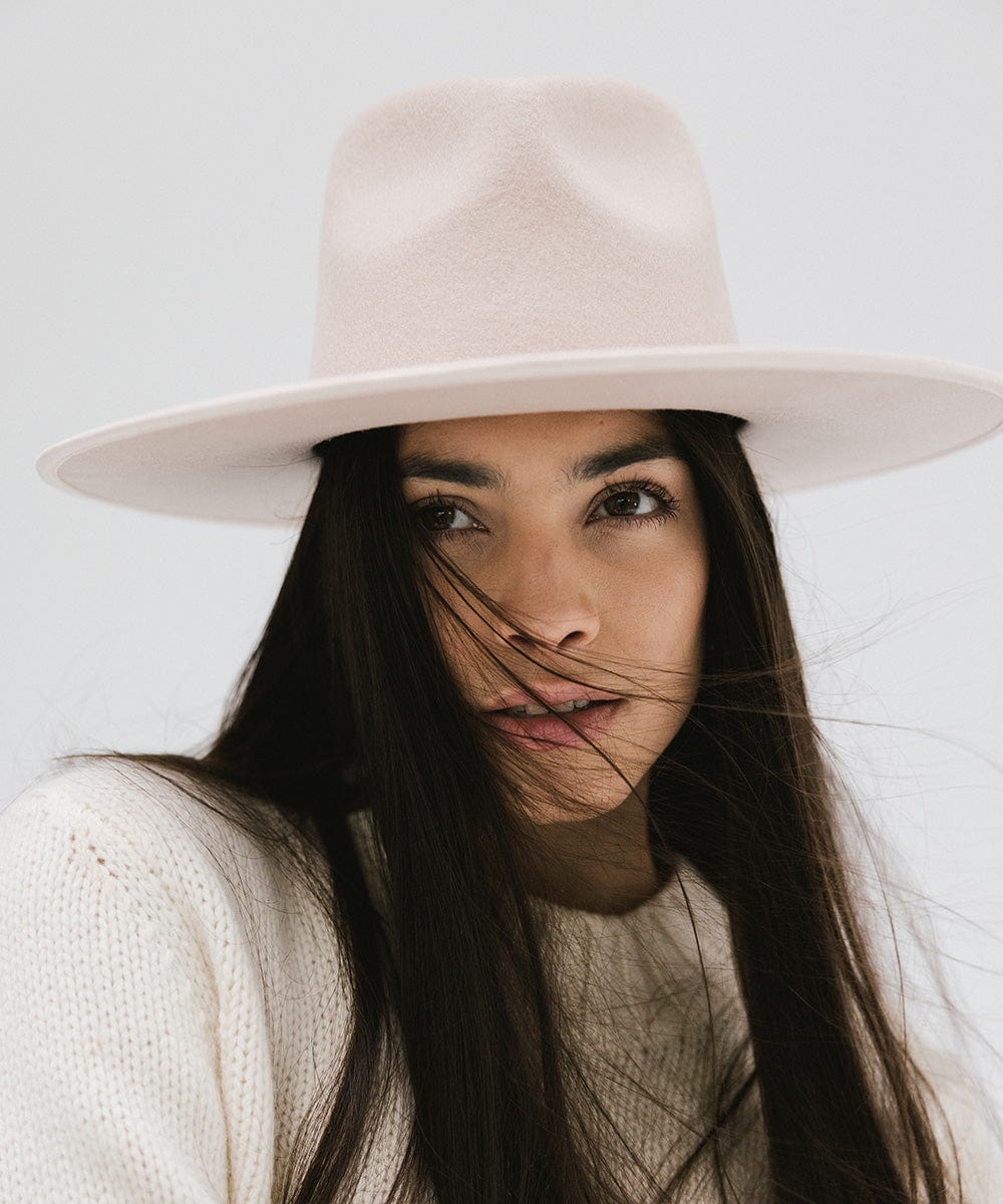 Woman wearing a pale nude colored fedora hat and a white sweater against a plain background #color_pale nude