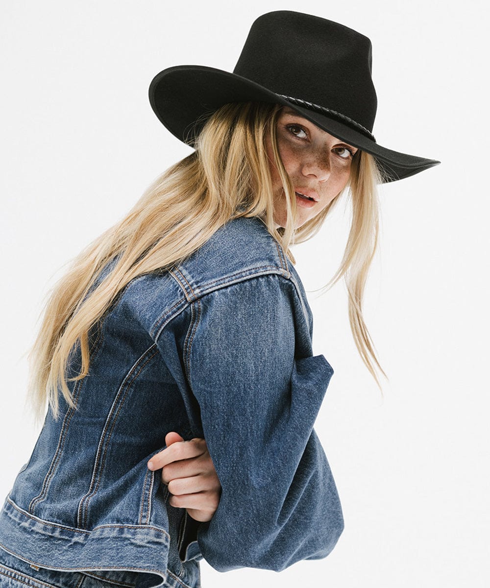 Woman wearing a black felt western hat and a denim shirt, posing sideways against a white background #color_black
