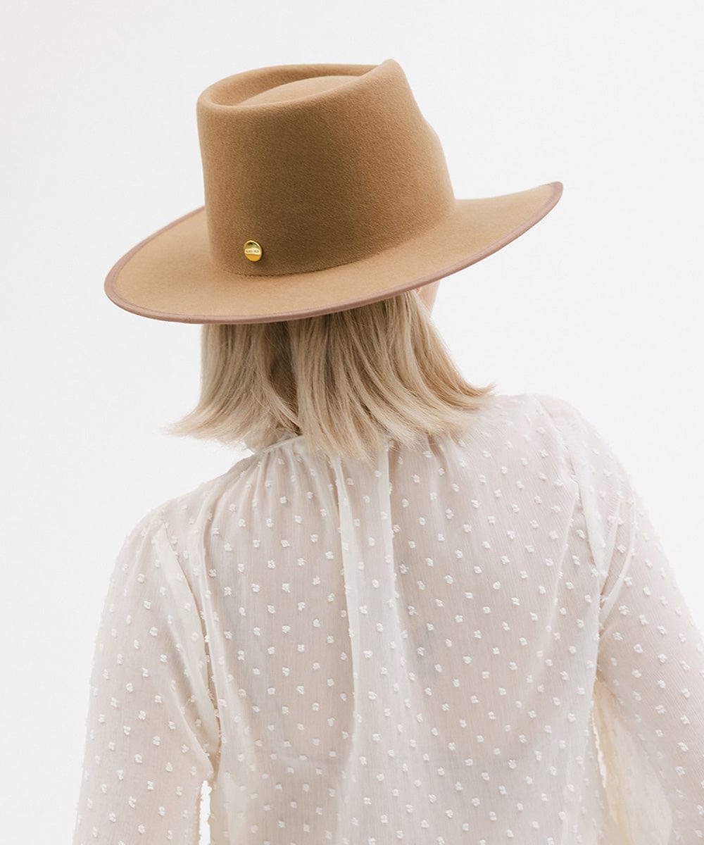 Person with short blonde hair wearing a brown felt western hat and a white top, facing behind against a white background #color_brown
