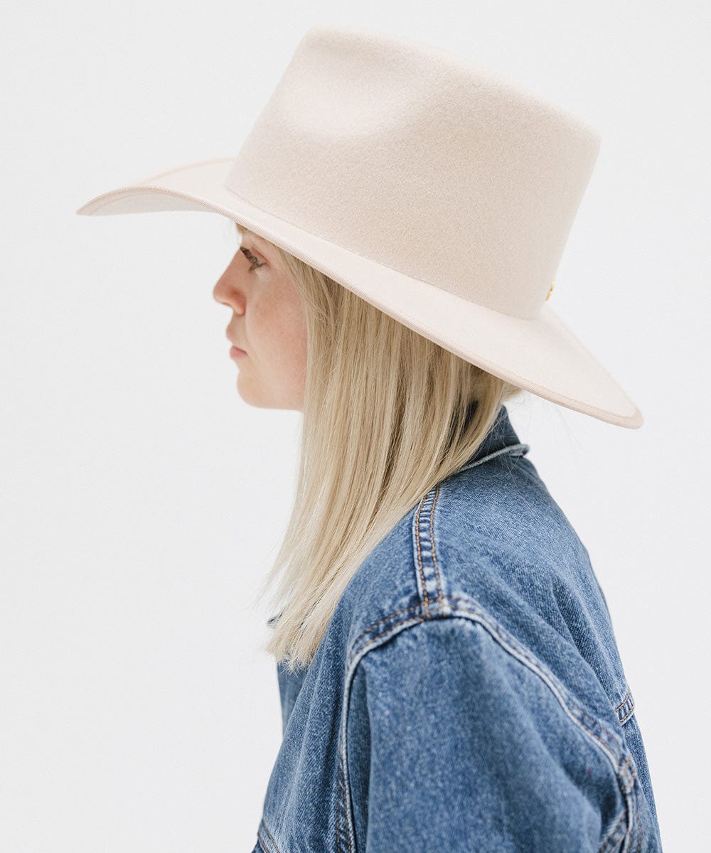 Woman wearing a cream felt western hat and a denim shirt, facing sideways against a white background #color_cream