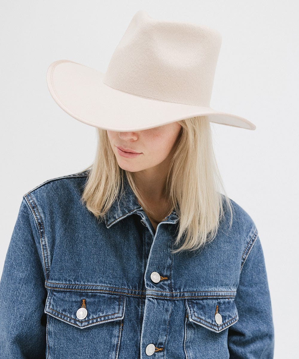 Woman wearing a cream felt western hat and a denim shirt, looking sideways against a white background #color_cream