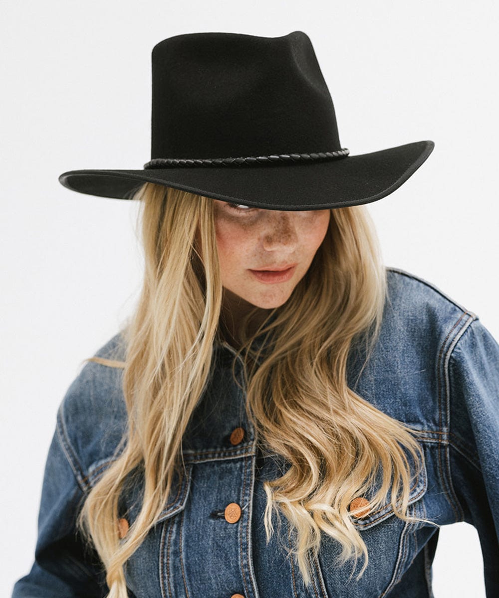 Woman wearing a black felt western hat and a denim shirt, looking sideways against a white background #color_black