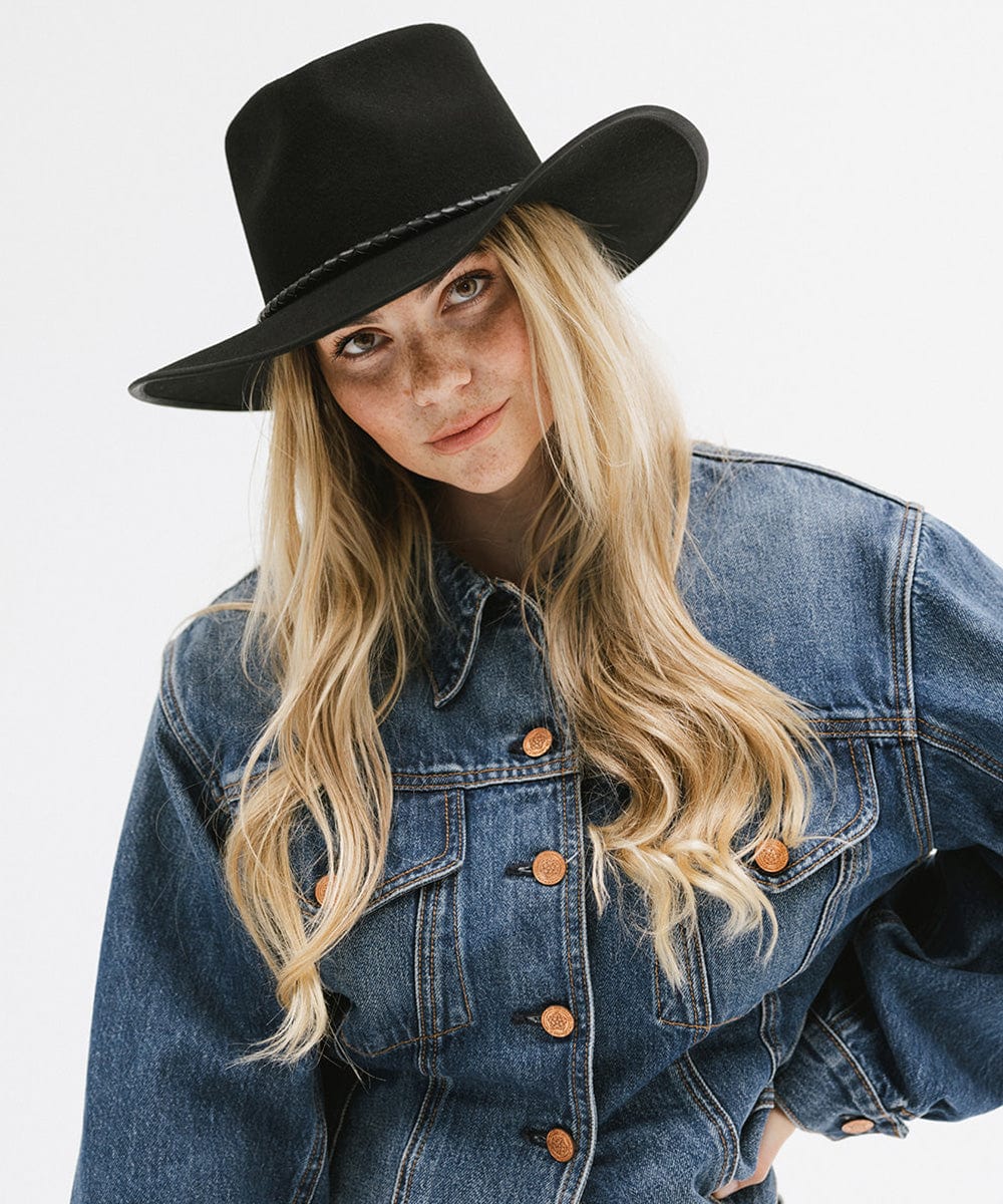 Woman with long blonde hair wearing a black felt western hat and a denim shirt against a white background #color_black