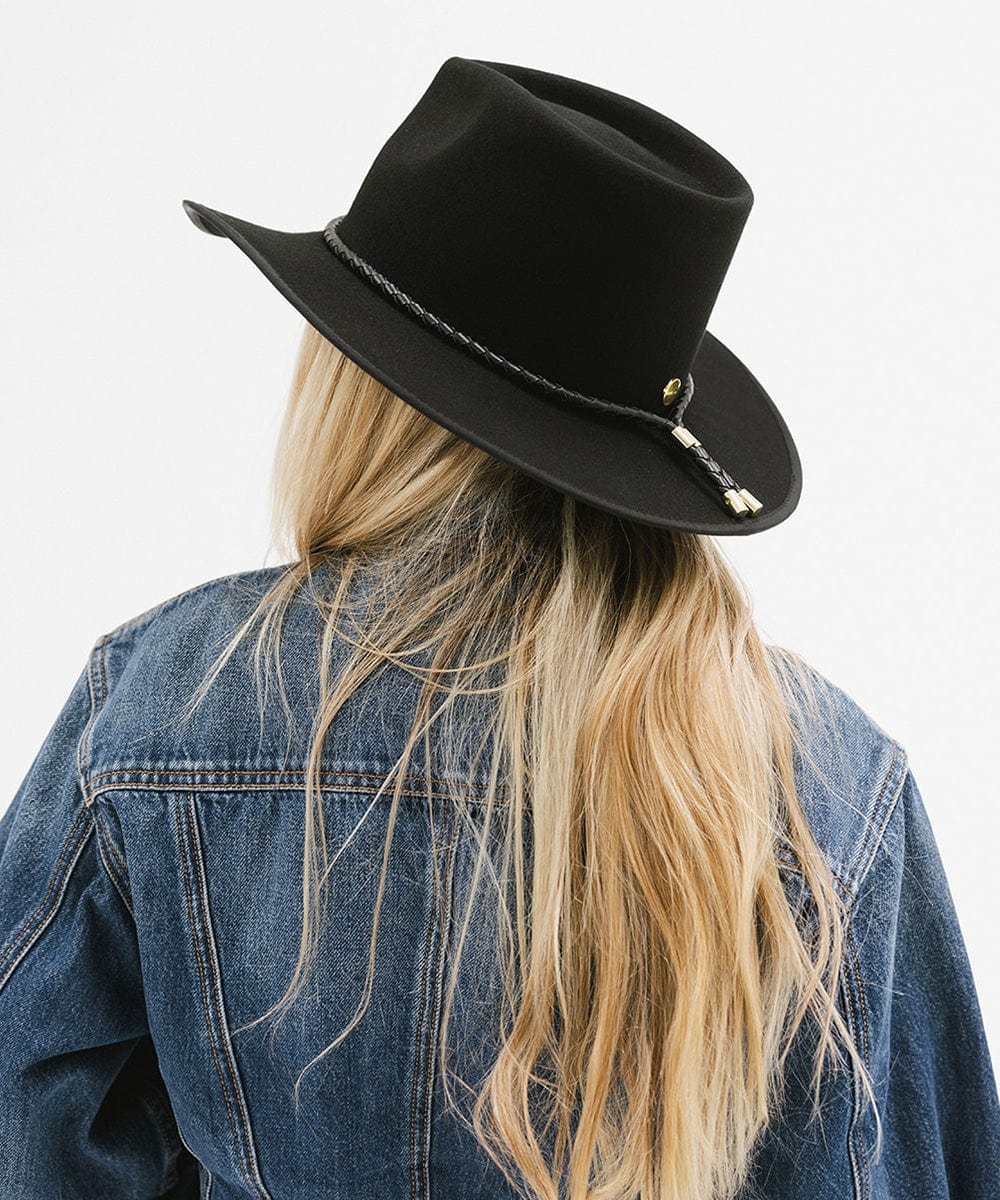 Woman with long blonde hair wearing a black felt western hat with a hat band and a denim shirt, facing behind against a white background #color_black