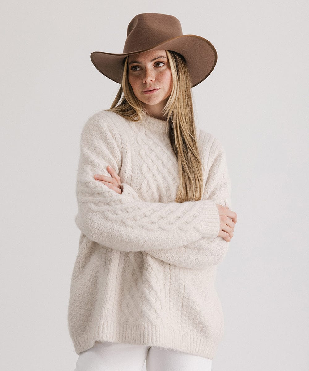 Woman with long hair wearing a chocolate brown felt western hat, a cream sweatshirt and white pants against a white background #color_chocolate