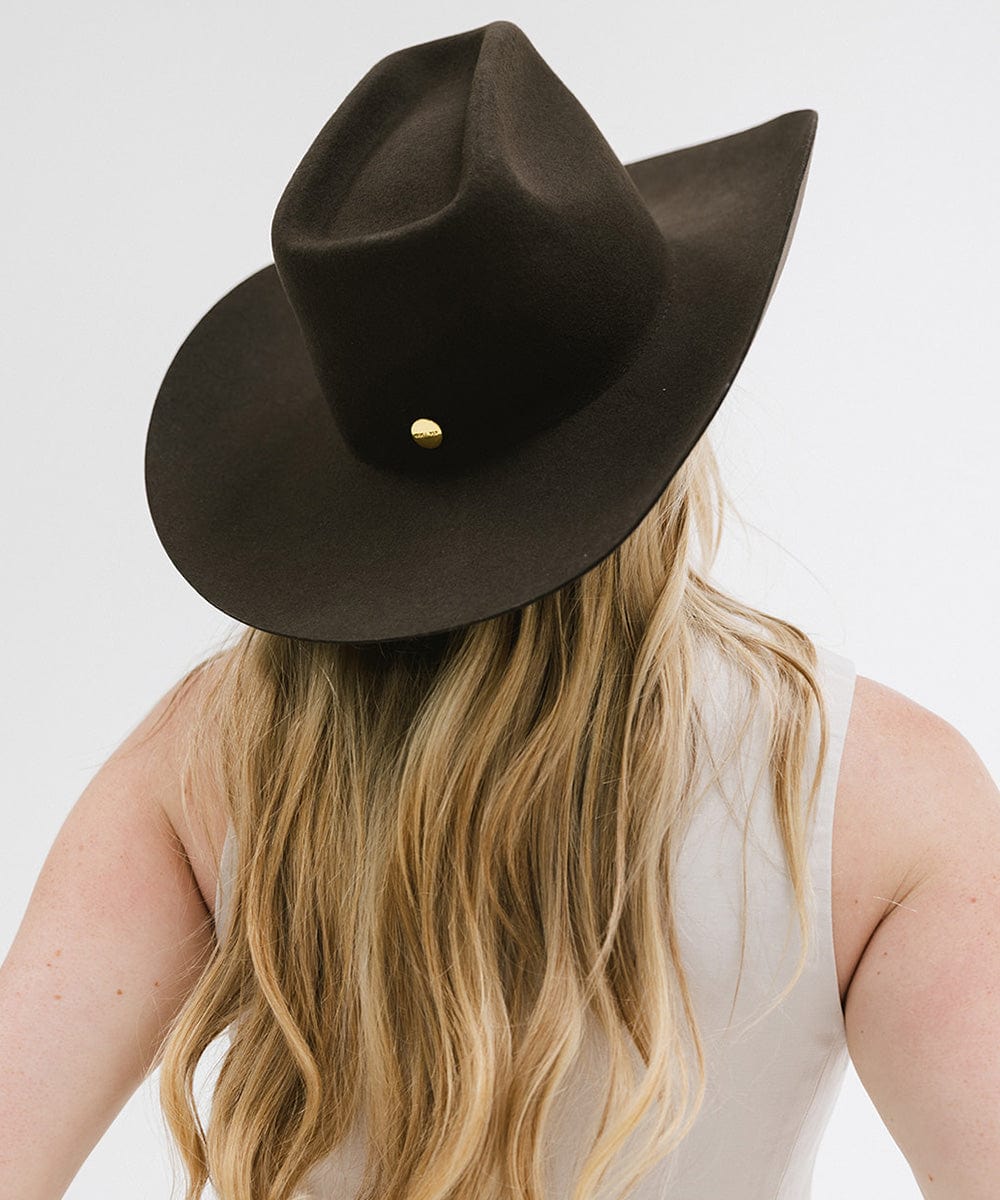 Person with long blonde hair wearing a dark brown cowboy hat  facing behind against a plain background #color_dark brown