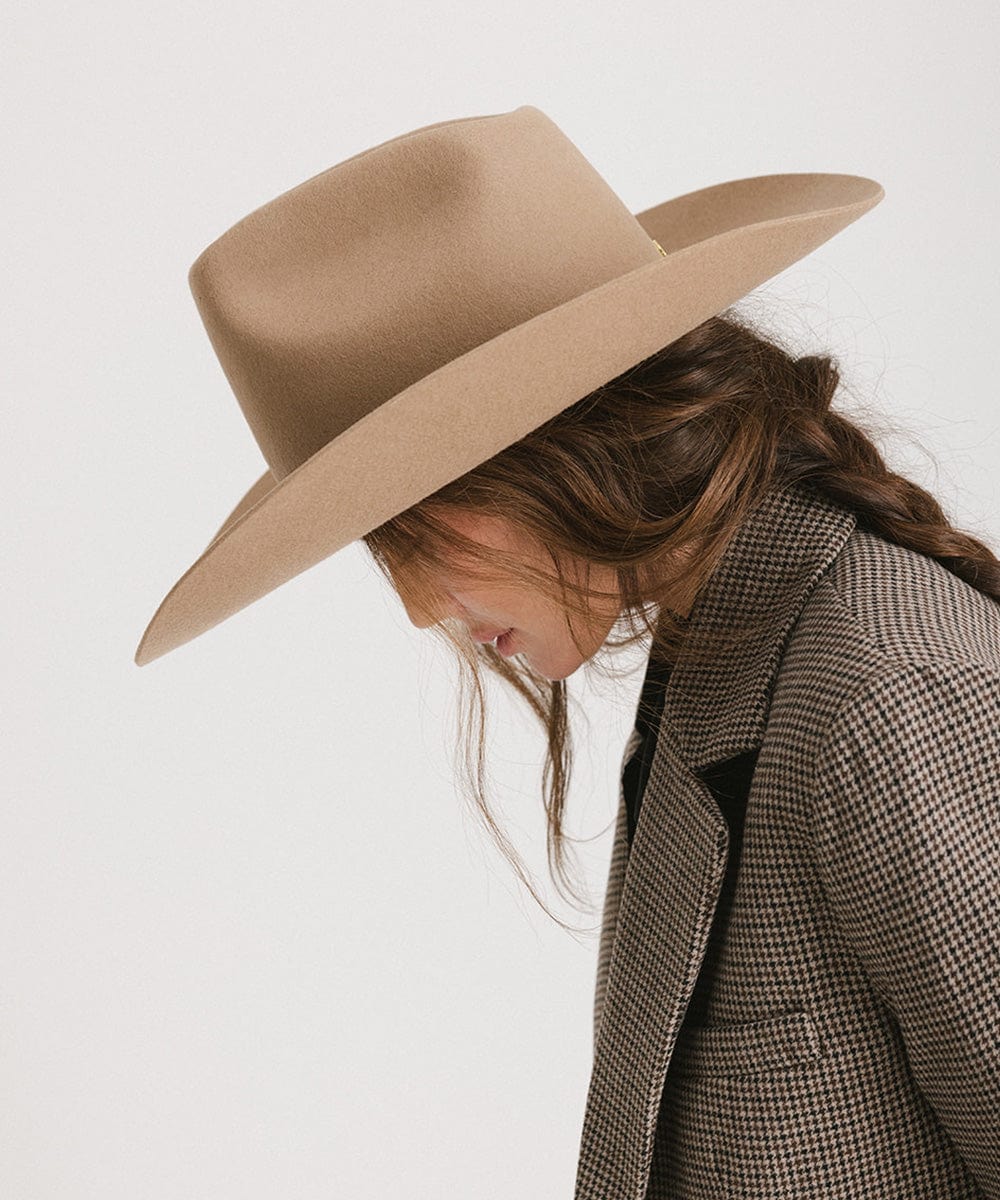 Woman wearing a brown cowboy hat and a blazer facing towards the right side against a plain background #color_brown