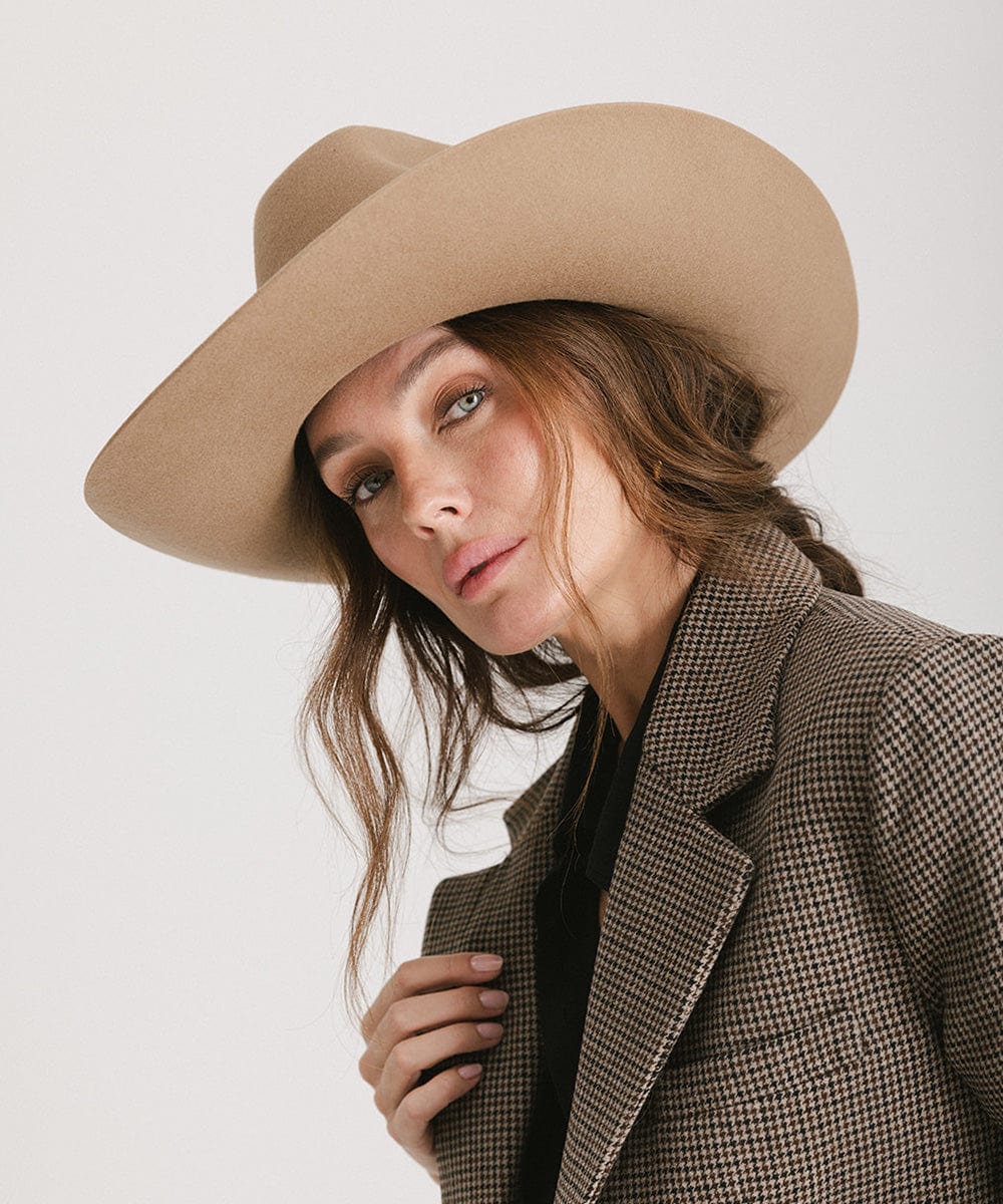 Woman wearing a brown cowboy hat and a blazer, posing against a plain background #color_brown