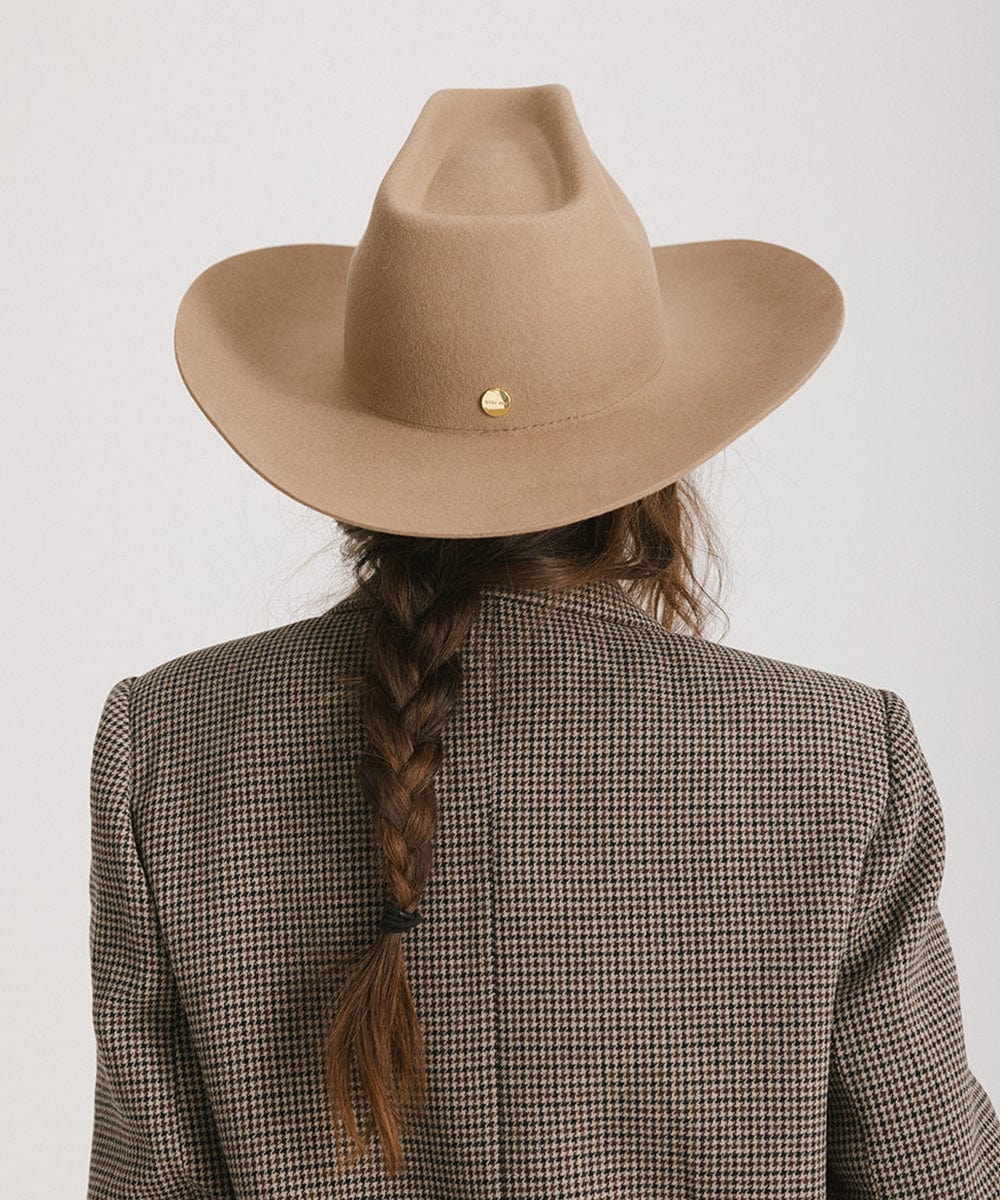 Person with a ponytail wearing a brown cowboy hat and a blazer, facing behind against a plain background #color_brown