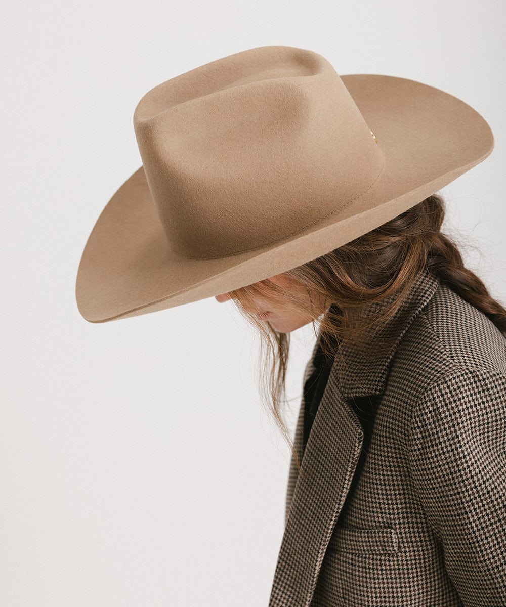 Woman wearing a brown cowboy hat and a blazer, looking down against a plain background #color_brown