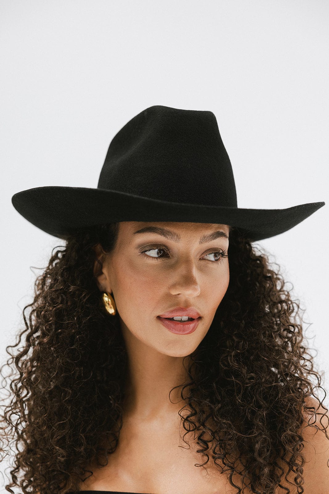 Woman with curly hair wearing a black cowboy hat against a plain background #color_black