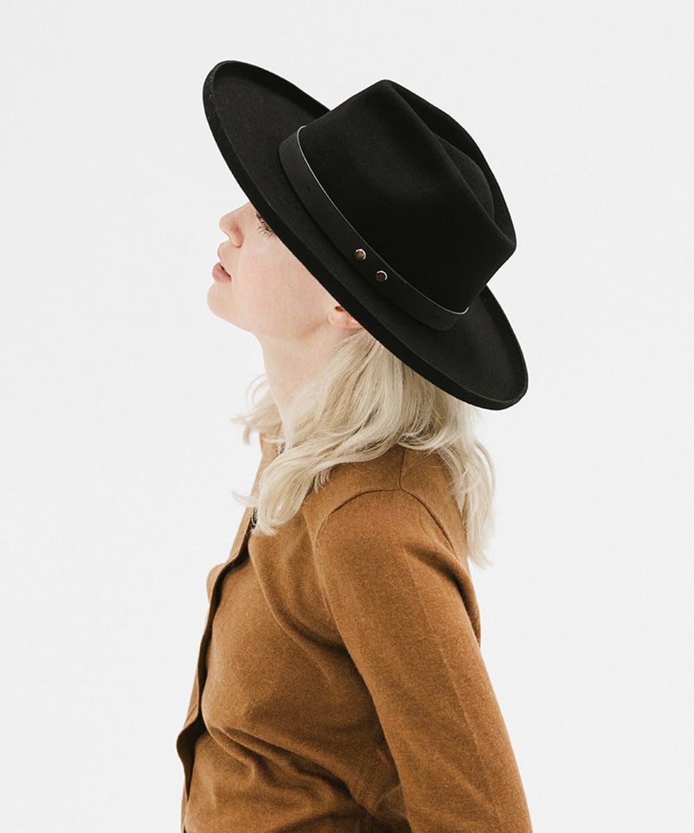 Woman wearing a black felt fedora hat with a hat band and a brown sweater, facing sideways against a plain background #color_black