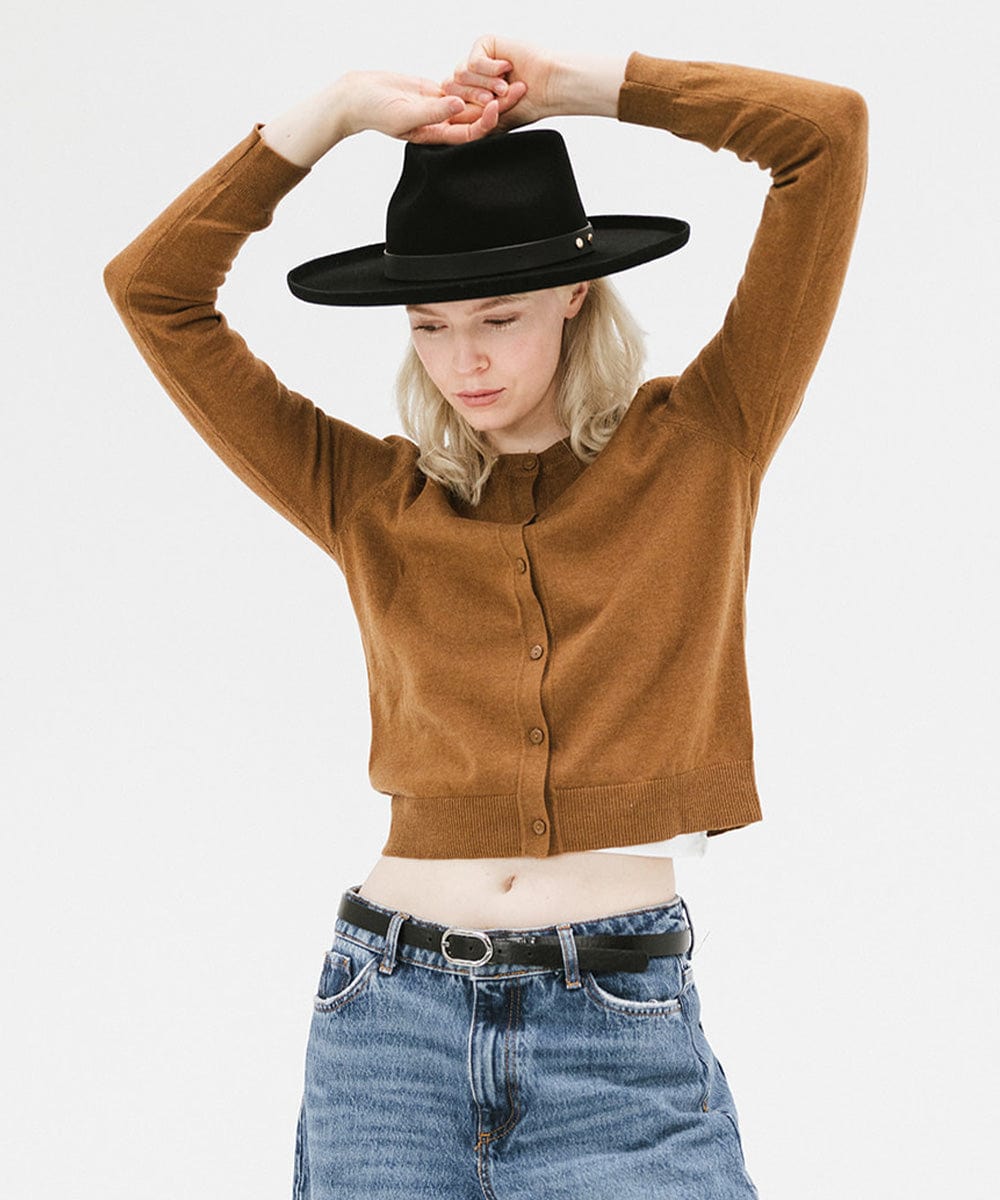 Woman wearing a black felt fedora hat with a hat band, a brown sweater, black belt and blue jeans against a plain background #color_black