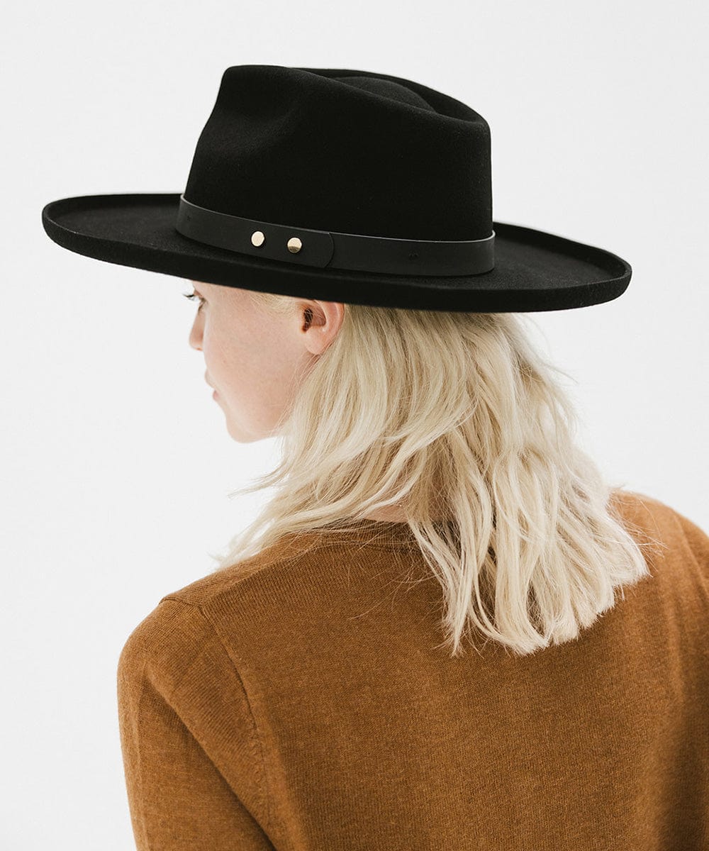 Woman wearing a black felt fedora hat with a hat band and a brown sweater, facing behind against a plain background #color_black