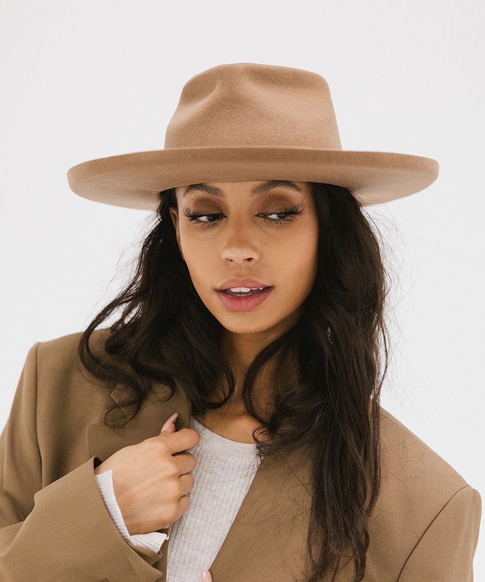 Woman wearing a tan felt fedora hat and a brown coat against a plain background #color_tan