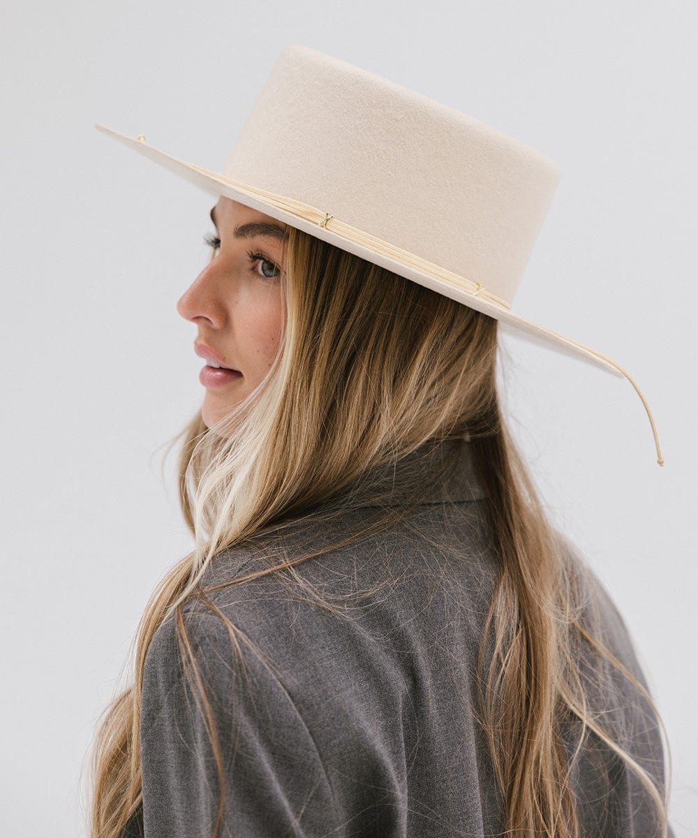 Woman wearing a cream Maise classic flat brim hat with a hat band and a grey blazer, posing sideways  against a plain background #color_cream