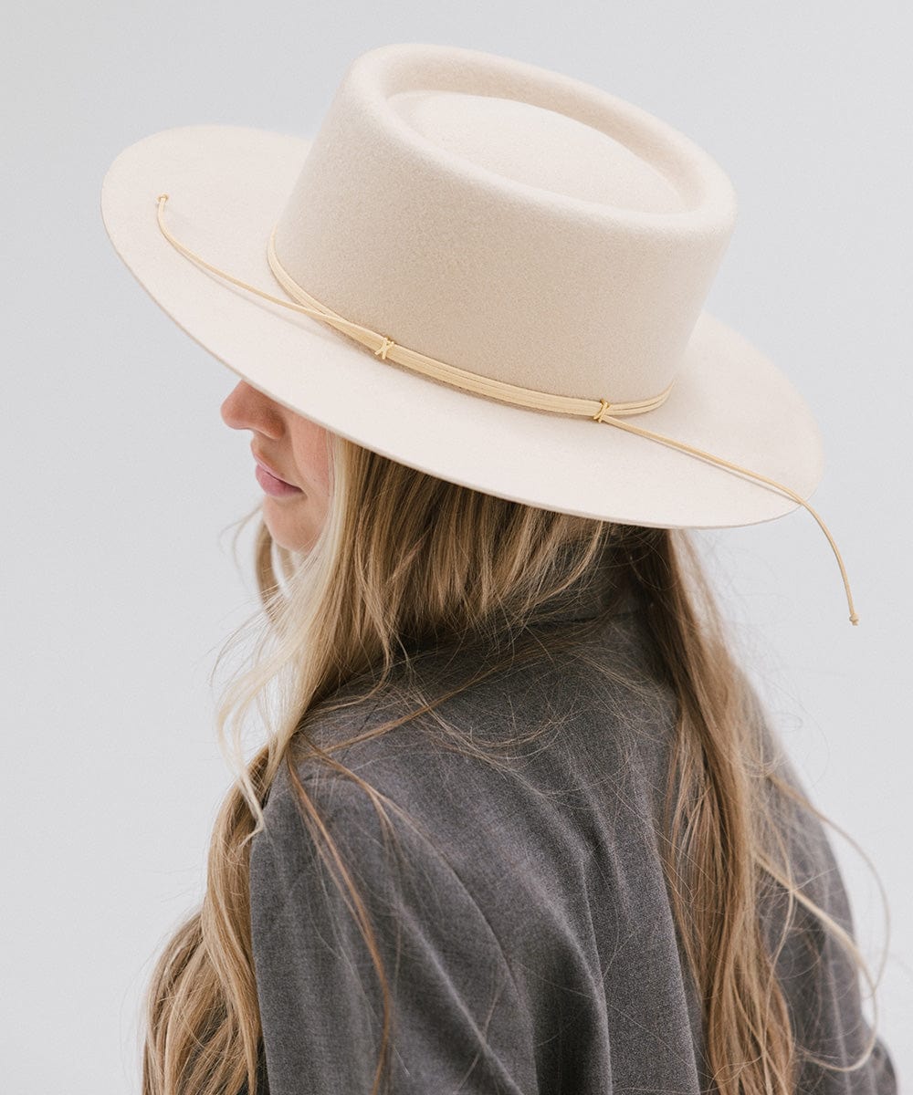 Woman wearing a cream Maise classic flat brim hat with a hat band and a grey blazer, facing sideways  against a plain background #color_cream