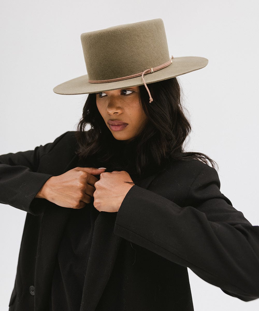 Woman wearing an aloe colored Maise classic flat brim hat with a hat band and a black blazer, posing against a plain background #color_aloe 