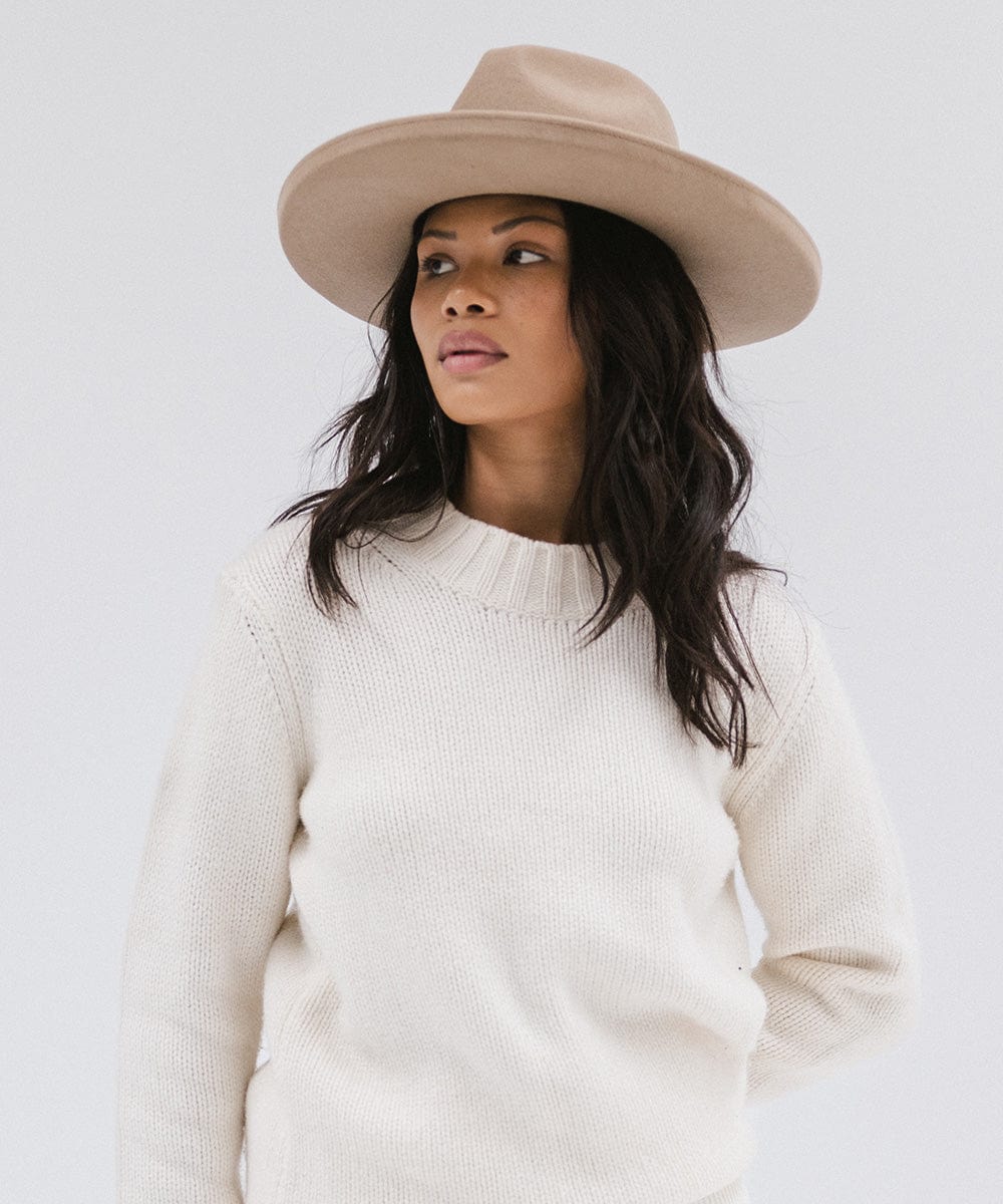 Woman wearing a tan pencil brim felt fedora hat and a white sweatshirt, looking sideways against a white background #color_tan