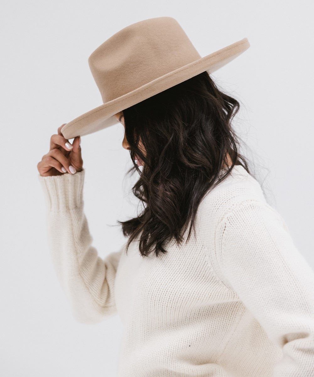 Woman wearing a tan pencil brim felt fedora hat and a white sweatshirt, facing sideways against a white background #color_tan