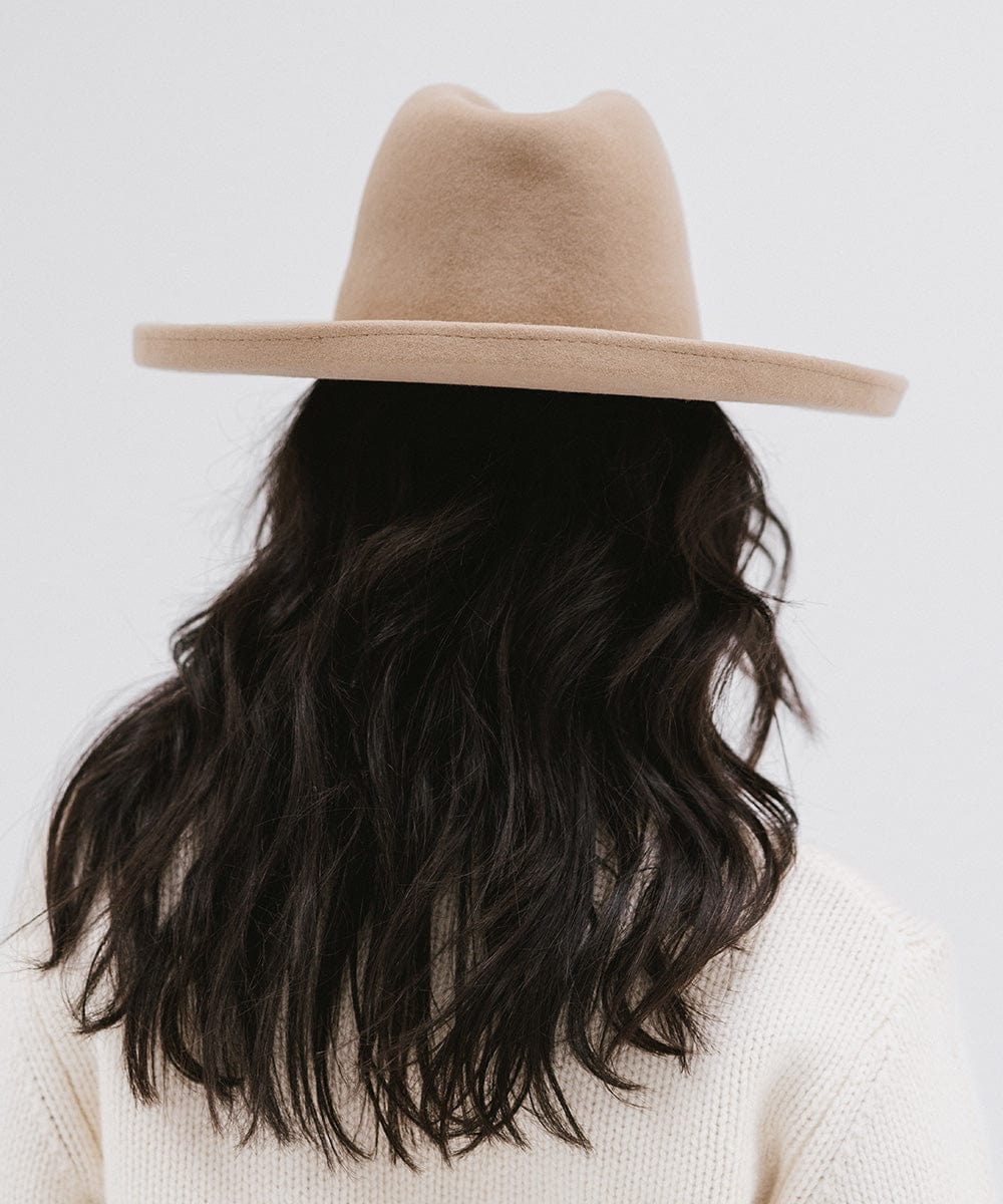 Woman wearing a tan pencil brim felt fedora hat and a white sweatshirt, facing behind against a white background #color_tan