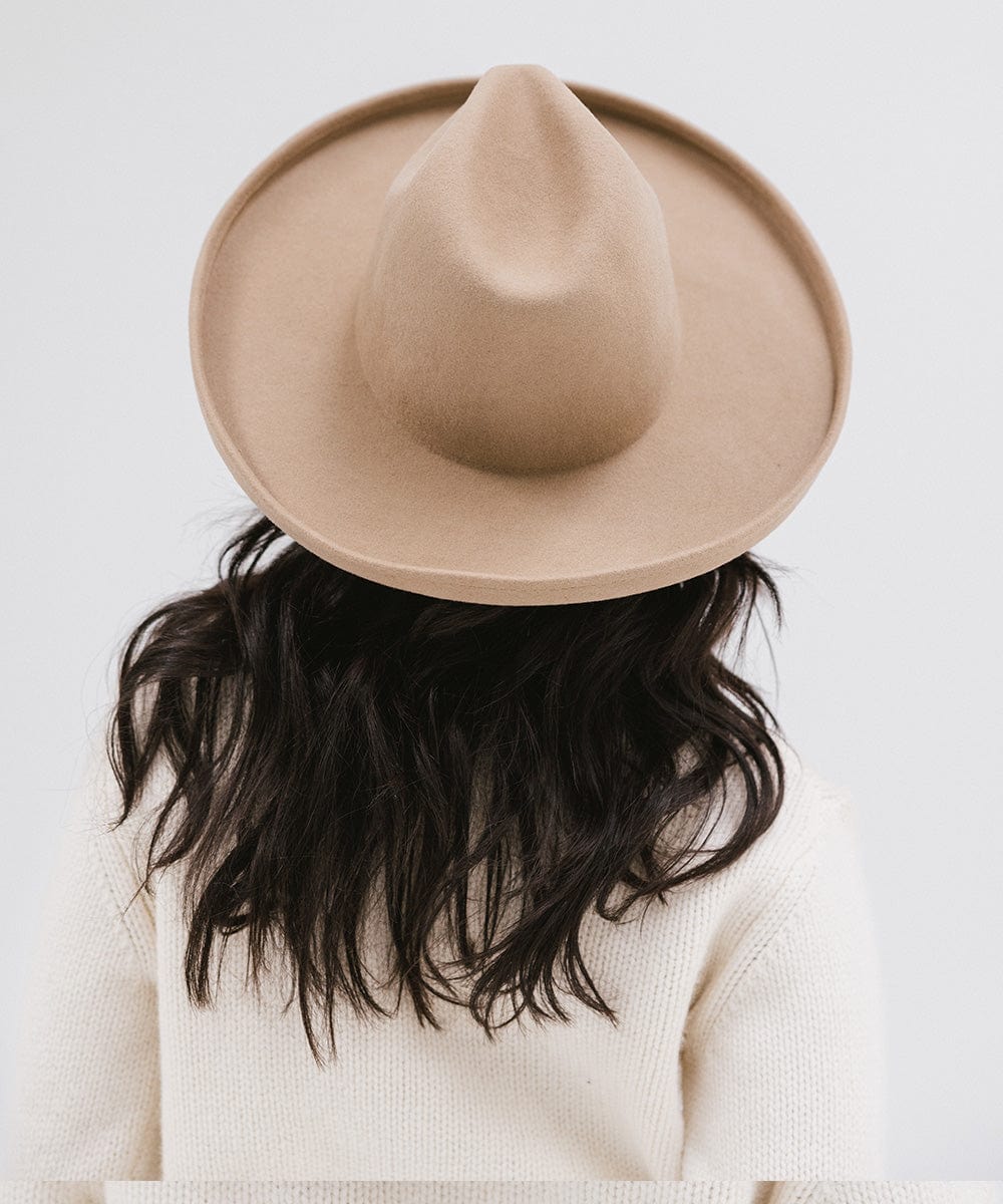 Woman wearing a tan pencil brim felt fedora hat and a white sweatshirt, facing behind against a white background #color_tan