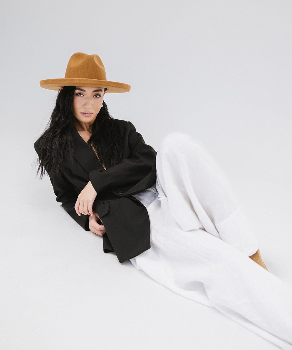 Woman wearing a cinnamon colored  pencil brim felt fedora hat, a black blazer and white pants against a white background #color_cinnamon