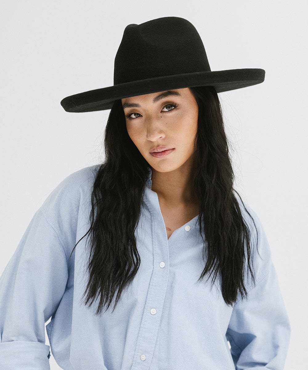 Woman wearing a black pencil brim felt fedora hat and a blue shirt against a white background #color_black
