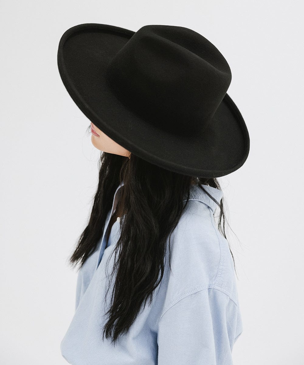 Woman wearing a black pencil brim felt fedora hat and a blue shirt, facing sideways against a white background #color_black