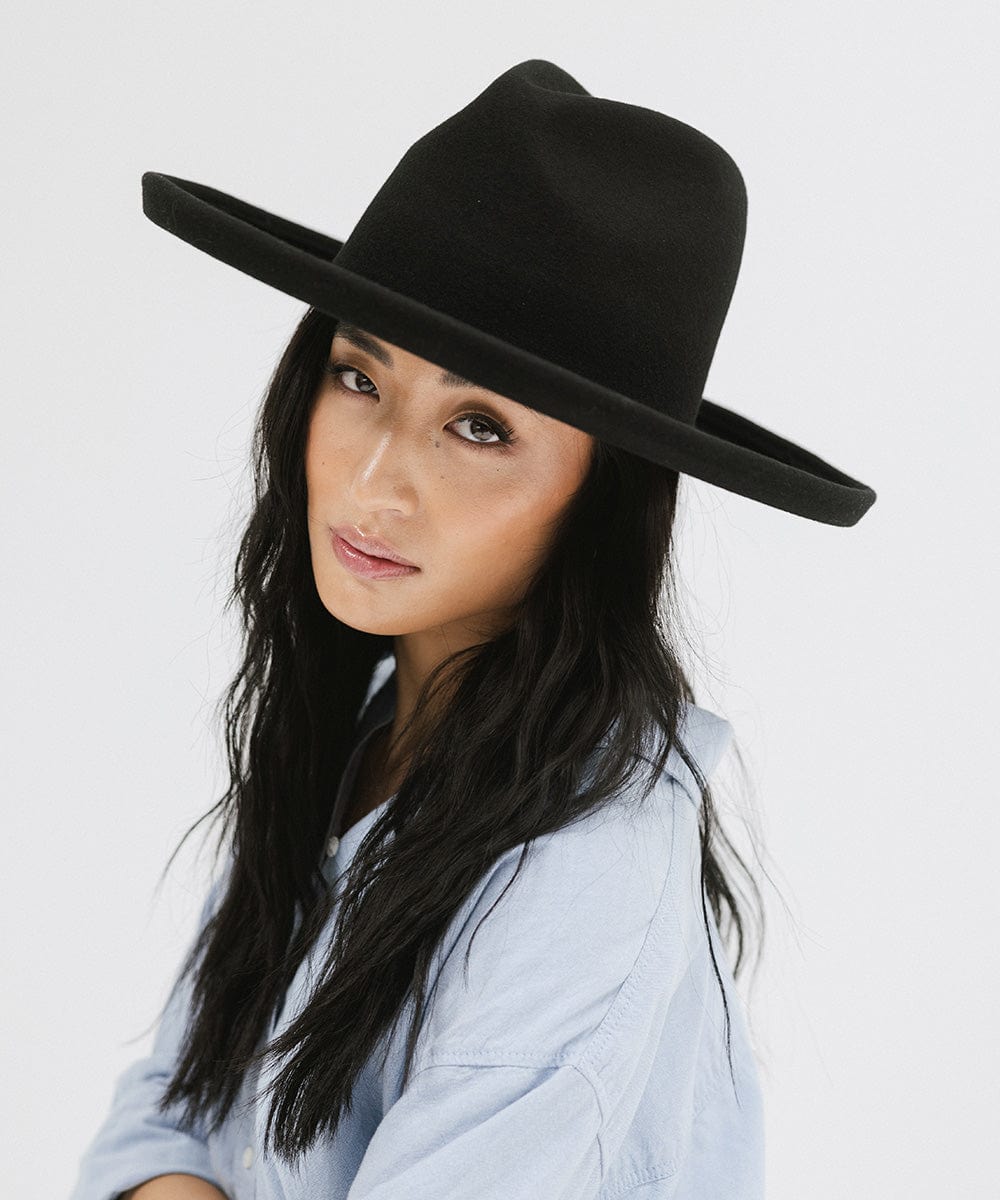 Woman wearing a black pencil brim felt fedora hat and a blue shirt, posing against a white background #color_black