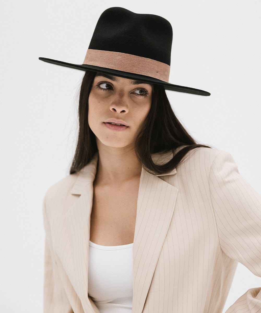 Woman wearing a black fedora hat with a brown band and a cream blazer  against a white background #color_black-brown