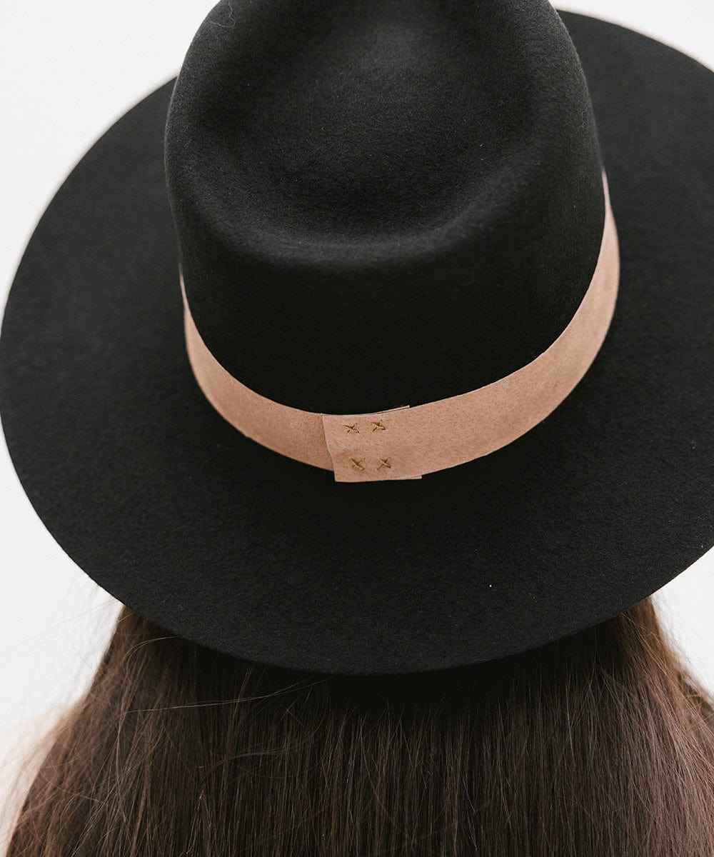 Black fedora hat with a brown band worn by a person against a white background #color_black-brown