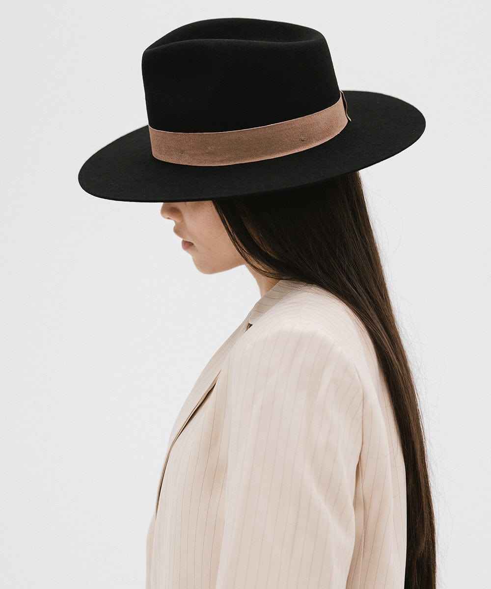 Person wearing a black fedora hat with a brown band and a cream blazer, facing sideways against a white background #color_black-brown