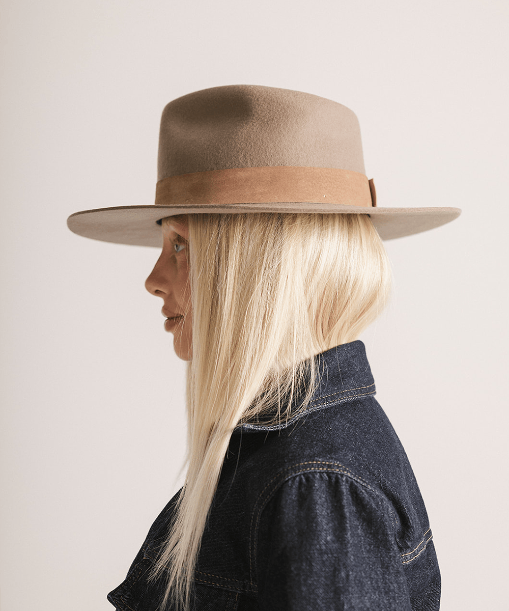 Woman wearing a brown fedora hat with a band against a plain background #color_brown