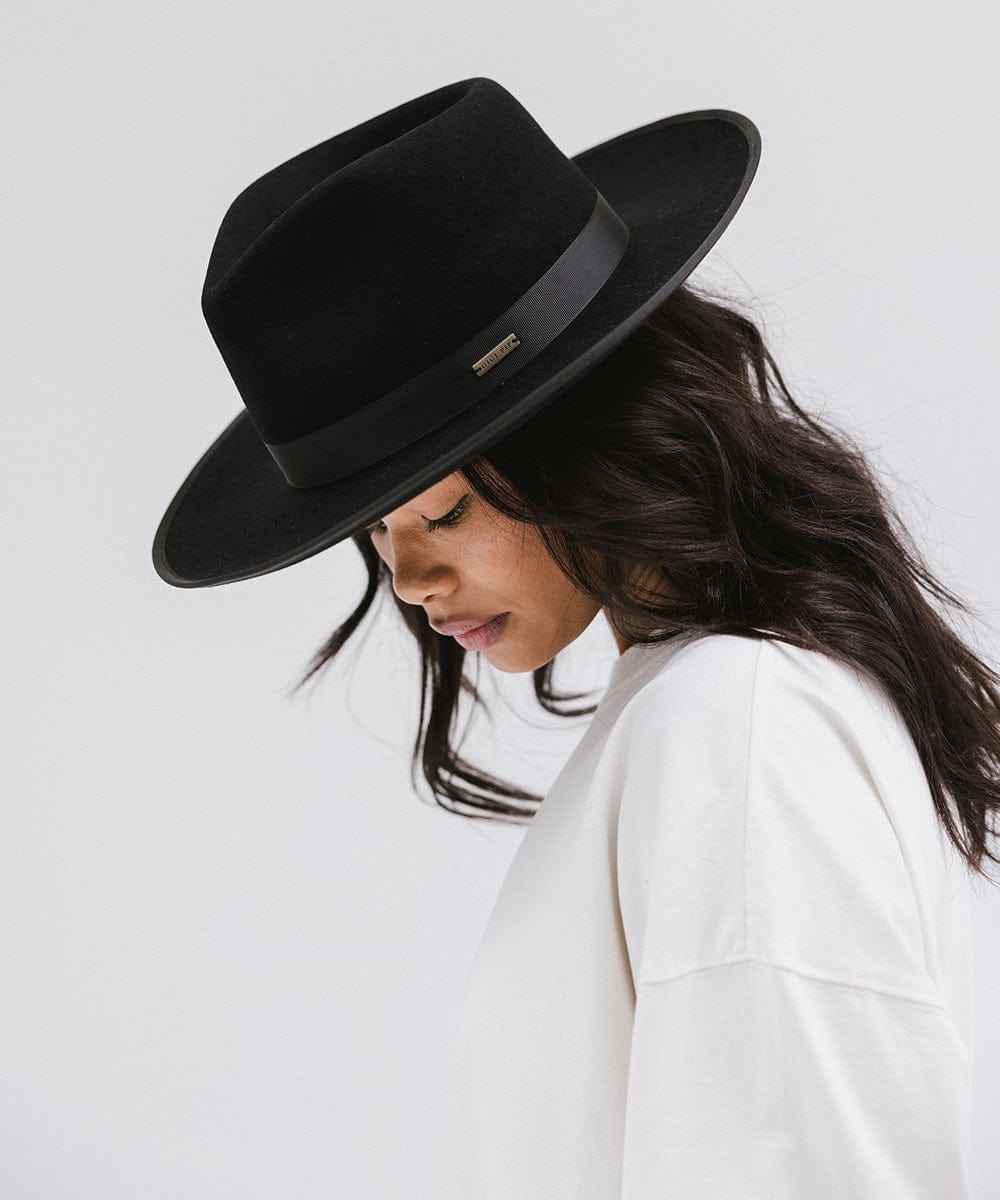 Woman wearing a black fedora hat with a band and a white t-shirt, looking down against a plain background #color_black