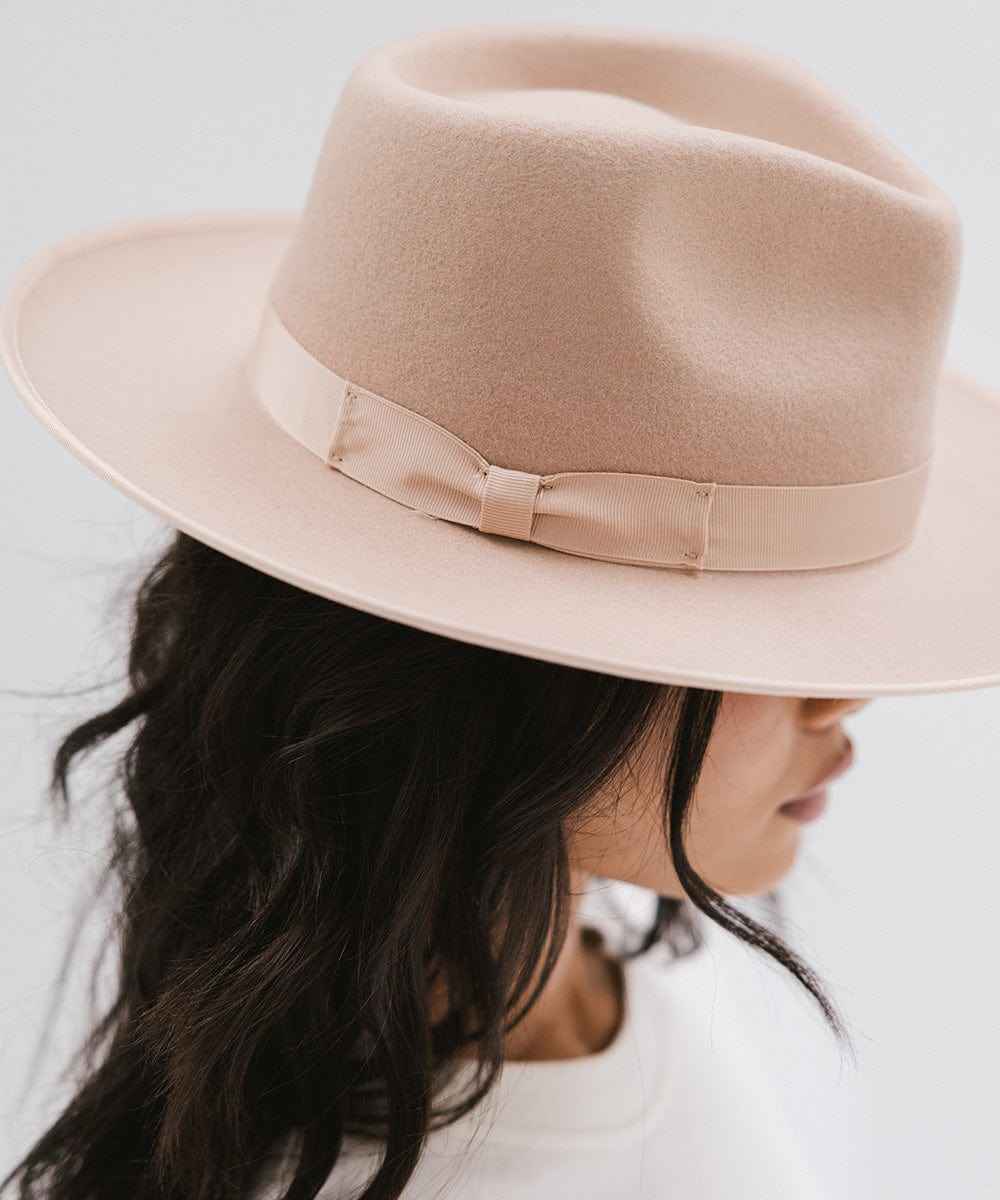 Woman wearing a nude fedora hat with a band facing sideways against a plain background #color_nude