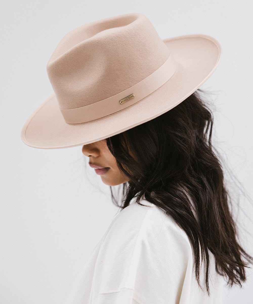Woman wearing a nude fedora hat with a band and a white t-shirt, facing sideways against a plain background #color_nude