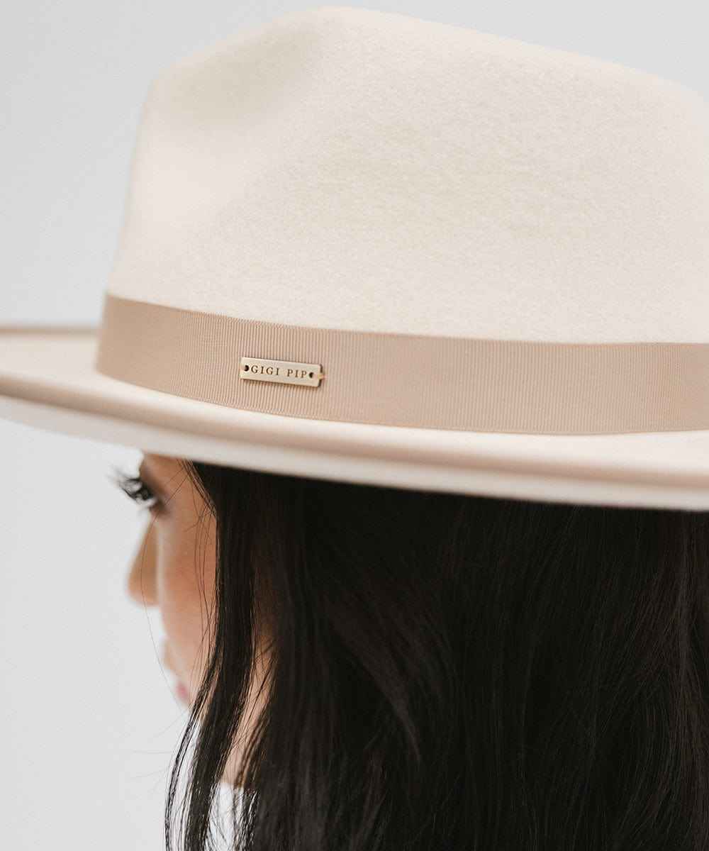 Woman wearing a white and taupe colored fedora hat with a taupe band against a plain background #color_white-taupe