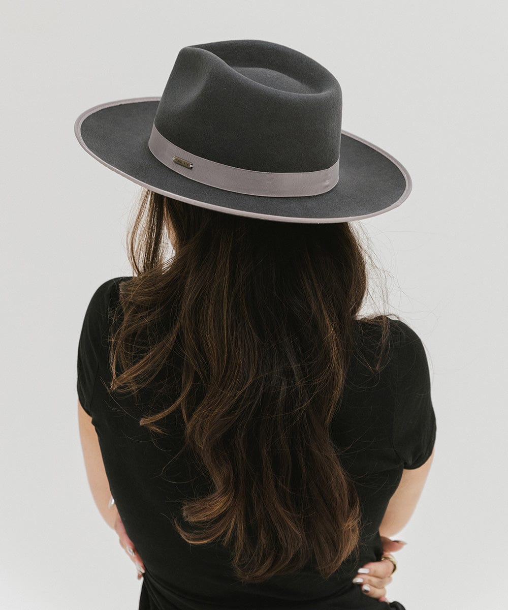 Woman wearing a dark grey fedora hat with a band and a black t-shirt, facing behind against a plain background #color_dark grey