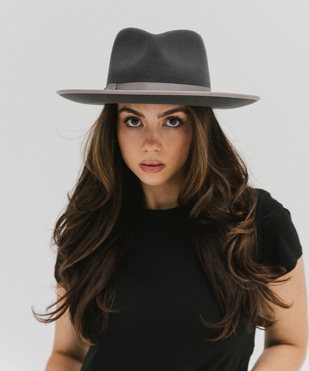 Woman wearing a dark grey fedora hat with a band and a black t-shirt against a plain background #color_dark grey