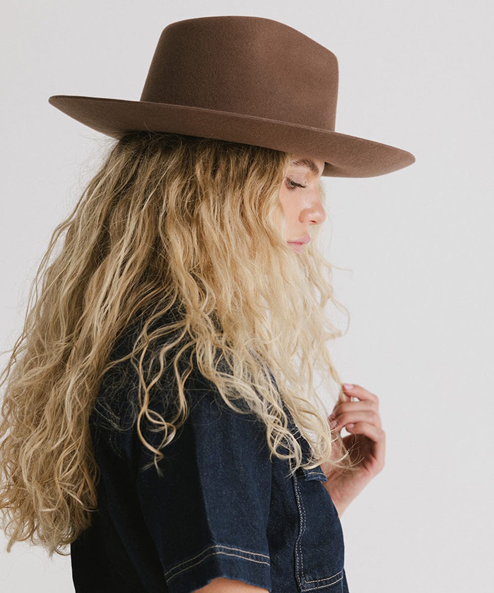 Woman with long blonde hair wearing a chocolate colored Rowan Wide Brim Fedora Hat and a denim shirt, facing sideways against a plain background #color_chocolate
